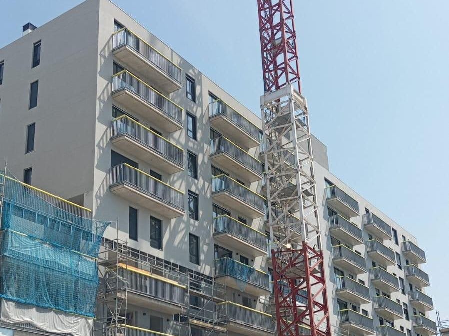 Bloque de viviendas de obra nueva en Badalona con la fachada acabada en mortero acrílico claro, balcones corridos con barandilla metálica y la grúa todavía montada