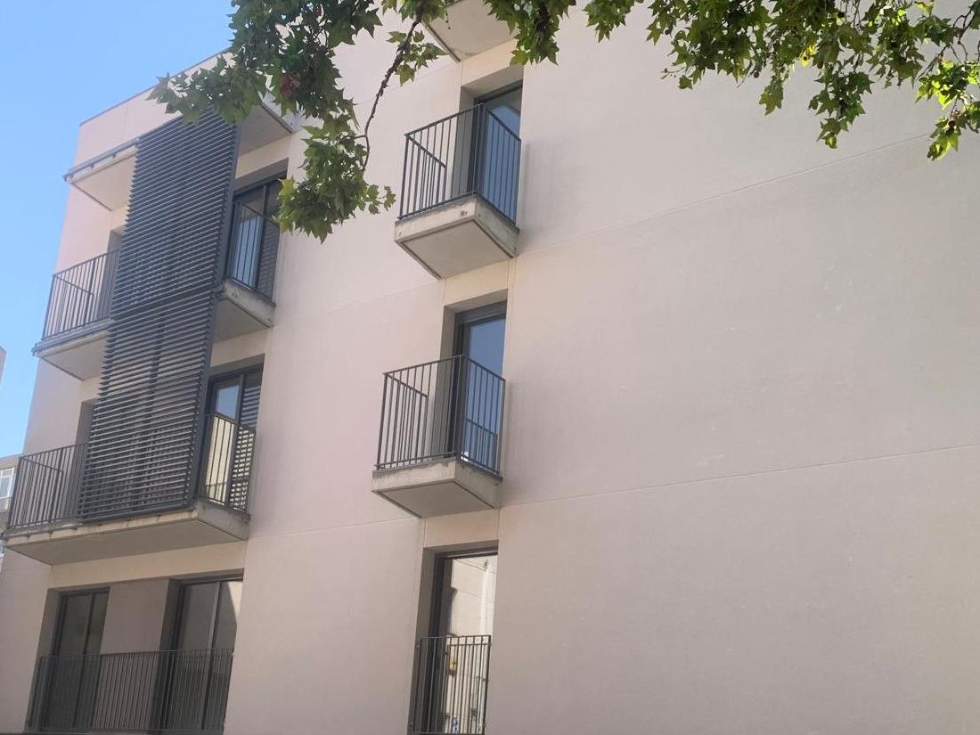 Bloque de viviendas en Sabadell con la fachada acabada en mortero monocapa en tono claro, balcones con barandilla metálica y lamas de protección solar