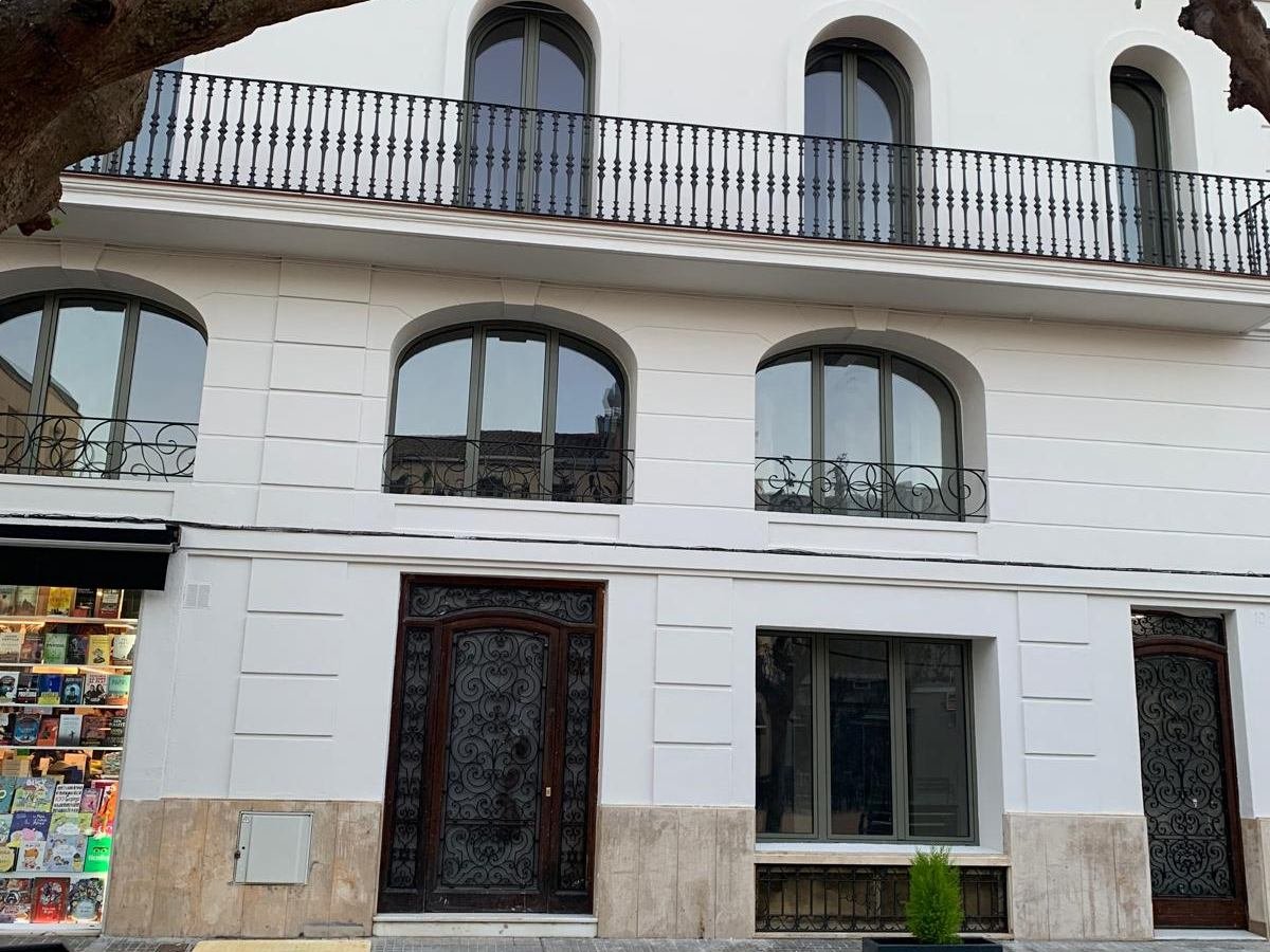La misma fachada vista de frente, con el revestimiento blanco recuperado, la balaustrada de la balconada, las ventanas de arco y la puerta de hierro forjado