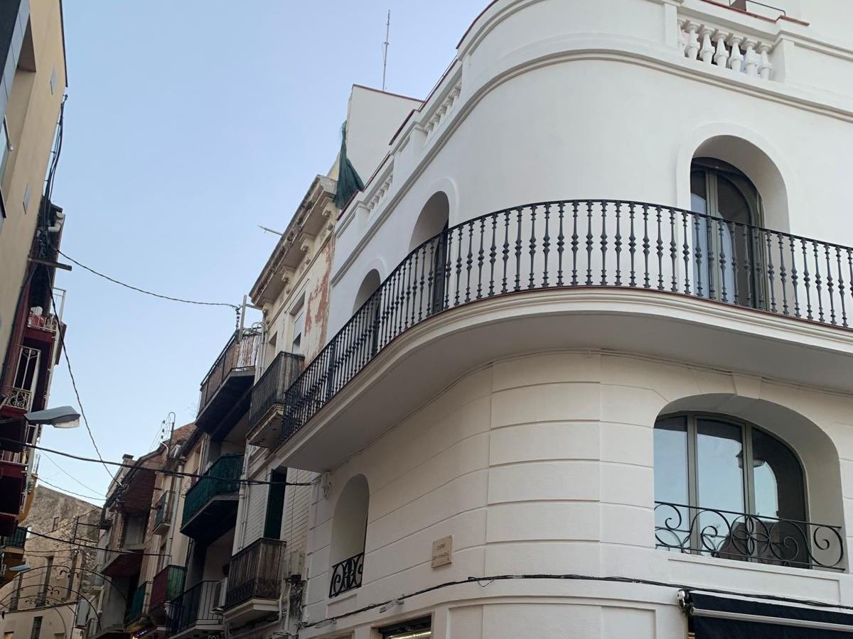 Edificio de esquina en Sant Feliu de Codines con la fachada rehabilitada: revestimiento blanco, balconada curva con barandilla de hierro torneado y ventanas de arco