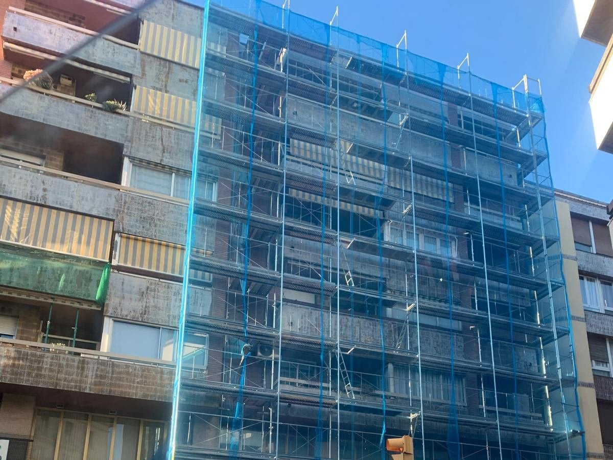 El andamio montado en toda la altura de la fachada y cubierto con red de protección azul, durante la rehabilitación, junto a un edificio vecino sin rehabilitar