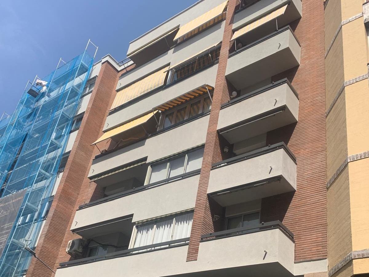 Fachada rehabilitada de un bloque de viviendas en Manresa, con el revestimiento nuevo, las pilastras de ladrillo y los balcones; a la izquierda, la parte todavía andamiada y cubierta con red