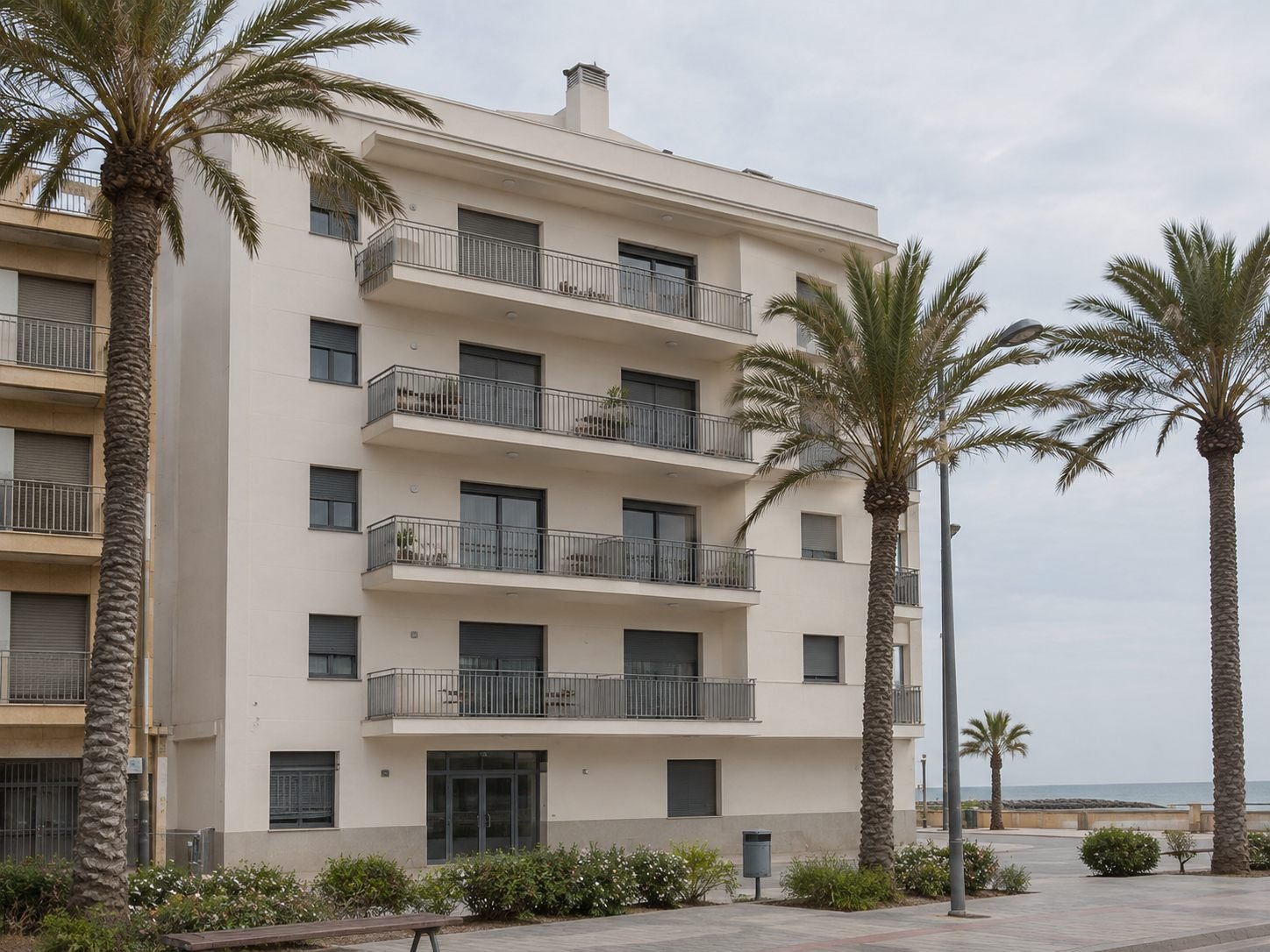 Edificio de viviendas en primera línea de mar, con la fachada acabada y palmeras y el paseo marítimo por delante