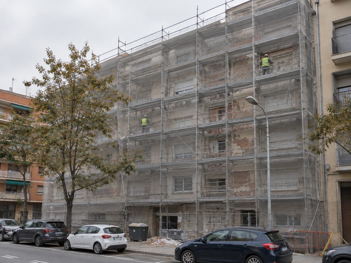 Bloque de viviendas en una calle de Granollers con el andamio y la malla montados en toda la fachada y el revestimiento picado a la vista